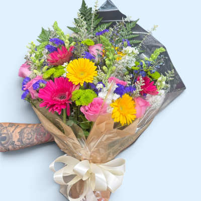 Mixed bouquet of pink, yellow, and purple flowers wrapped in paper with a ribbon