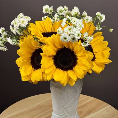 Sunflowers and white daisy-like flowers arranged in a white boot vase