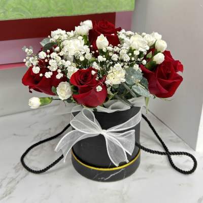 Red and white rose arrangement in a black round box with a white ribbon