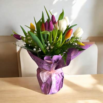 Bouquet of multicolored tulips wrapped in purple paper with a pink ribbon