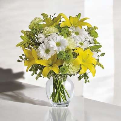 Yellow lilies and white daisies in a clear glass vase