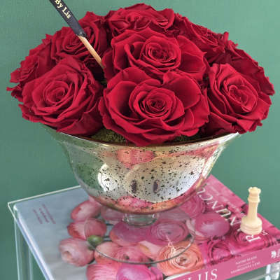Red roses arranged in a silver pedestal bowl with a black ribbon pick