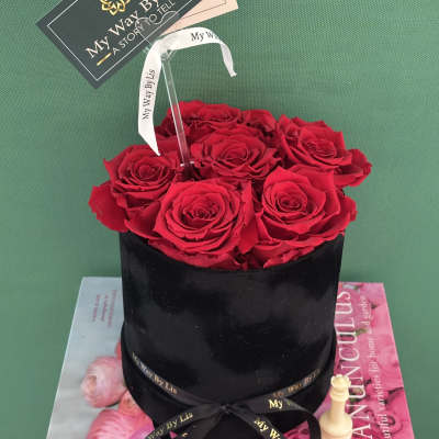 Red roses arranged in a black round box with a ribbon and card