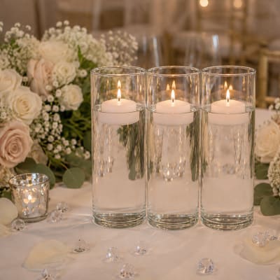 Three floating candles in glass cylinders on a floral table centerpiece