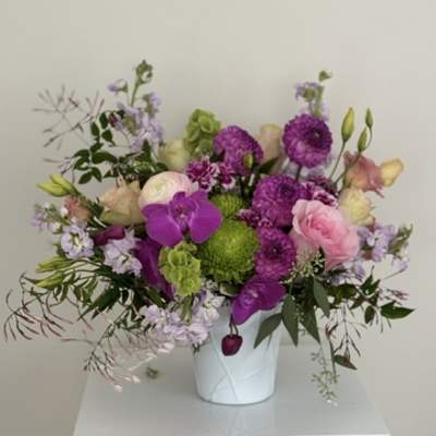 Mixed pink, purple, and green flowers arranged in a white vase