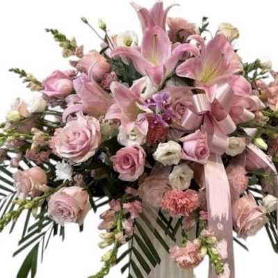 Pink floral spray with roses and lilies, accented by a pink ribbon