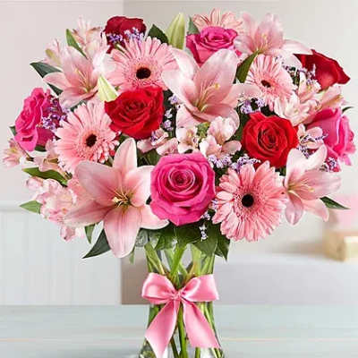 Pink and red bouquet of roses, lilies, and gerbera daisies in a glass vase