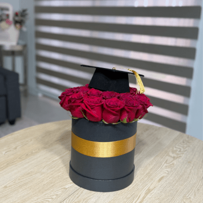 Red roses arranged in a black hat box with a graduation cap on top