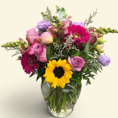 Mixed bouquet in a glass vase with sunflowers, roses, and pink gerberas