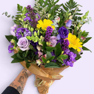 Hand-tied bouquet of purple and yellow flowers wrapped in brown paper