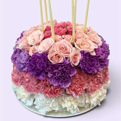 Round floral cake with pink roses, purple carnations, and white candles