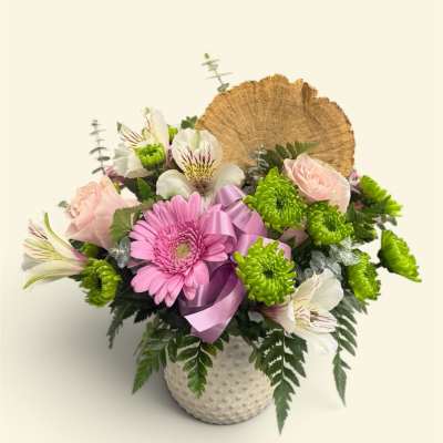 Pink gerbera and pale roses in a white textured vase with a ribbon