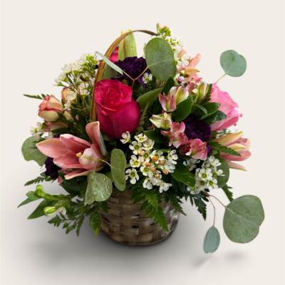 Basket arrangement of pink roses, lilies, and small white flowers