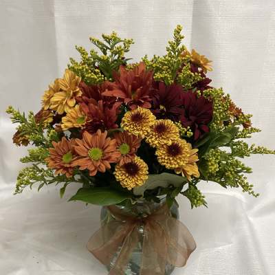 Autumn bouquet of orange, yellow, and burgundy flowers in a glass vase
