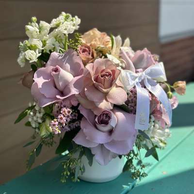 Pink and lavender rose bouquet in a white vase with a ribbon