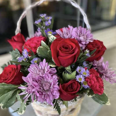 Basket of red roses and purple daisies with a white handle