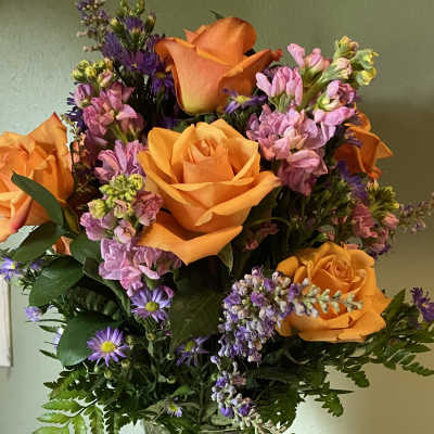 Orange roses and purple flowers in a clear glass vase