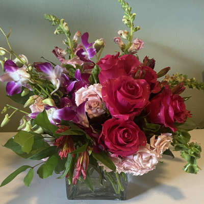 Pink roses and purple orchids arranged in a square glass vase