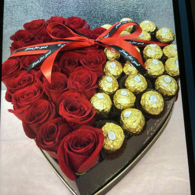 Heart-shaped box with red roses and gold-wrapped chocolates tied with a ribbon