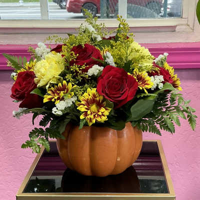 Pumpkin-shaped vase holding red roses and yellow flowers
