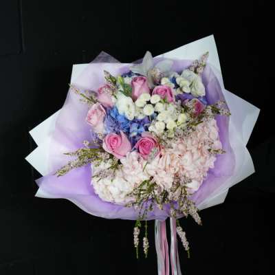 Bouquet of pink roses, hydrangeas, and white flowers wrapped in lavender paper