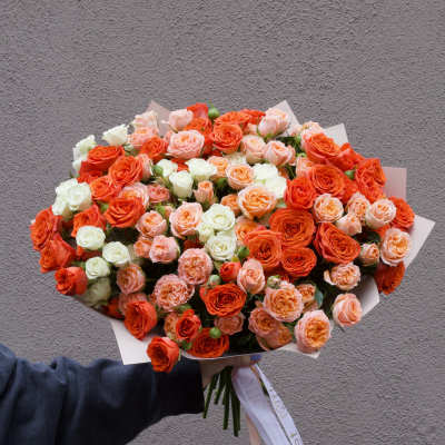Large bouquet of orange, peach, and white roses wrapped in paper