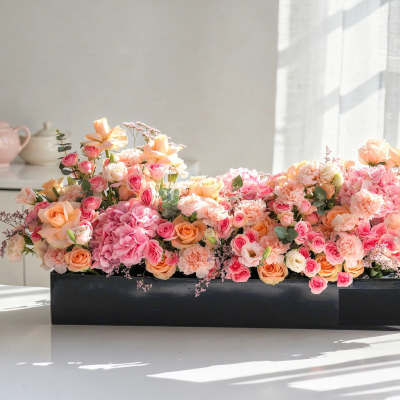 Low rectangular flower arrangement in a black box with pink and peach blooms