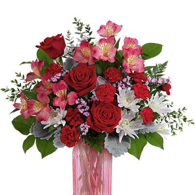 Red roses, pink alstroemeria, and white mums arranged in a tall pink glass vase