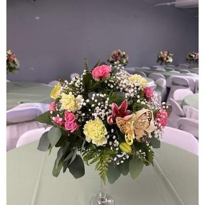 Tall round centerpiece of pink roses, yellow carnations, lilies, and baby's breath in a clear glass vase