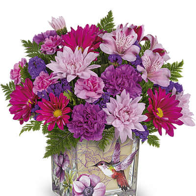Pink and purple mixed flower arrangement in a square glass vase with a hummingbird illustration