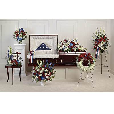 Patriotic red, white, and blue funeral flower set arranged around a casket with a folded American flag.