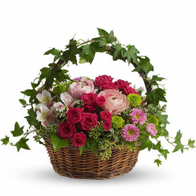 Low wicker basket of pink roses, ranunculus, and mixed blooms with an arching ivy handle