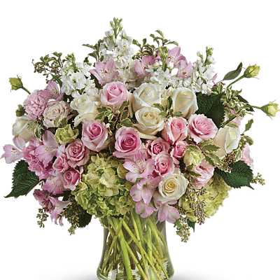 Large pastel bouquet of pink and white roses, hydrangeas, and other blooms in a clear glass vase