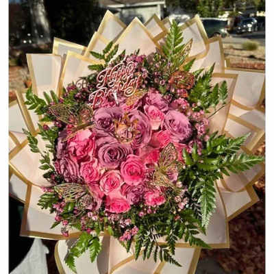 Large round bouquet of pink and lavender roses with birthday pick and butterflies in cream wrap