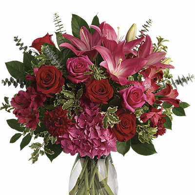 Pink lilies, red roses, and pink hydrangea arranged in a clear glass vase