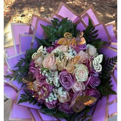 Hand-tied bouquet of lavender and cream roses with white filler flowers, wrapped in lilac paper with gold butterflies.