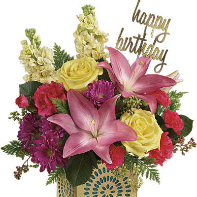 Bright arrangement of pink lilies, yellow roses and mixed blooms in a gold cube with a happy birthday pick