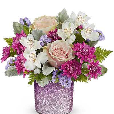 Short arrangement of pink roses, white alstroemeria, and purple mums in a textured lavender glass vase