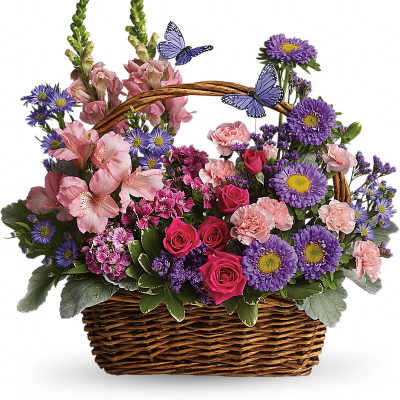 Wicker basket of pink roses, carnations and mixed purple flowers with two faux butterflies.