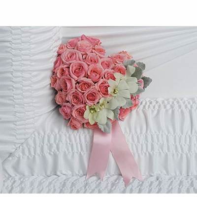 Heart-shaped pink rose arrangement with white orchids and pink ribbon on white ruched fabric.