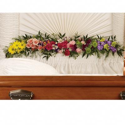 Multicolored floral spray with roses and daisies lining the interior of a white casket.