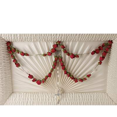 Red rosebud rosary garland draped inside an ivory casket lid with a silver cross.