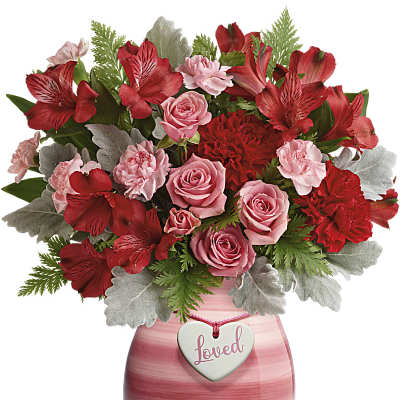 Red and pink roses, carnations, and alstroemeria in a pink vase with a heart tag