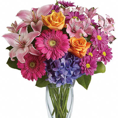 Mixed bouquet of pink lilies, gerberas, orange roses and purple hydrangea in a clear glass vase