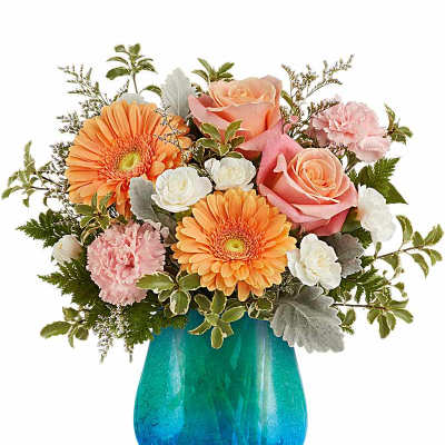 Peach gerbera daisies, pink roses, and white blooms arranged in a rounded blue glass vase.