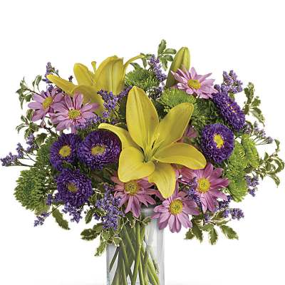 Mixed bouquet of yellow lilies and purple and pink daisies in a clear glass vase