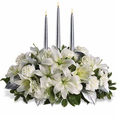Low centerpiece of white lilies and carnations with silver leaves and three tall silver taper candles