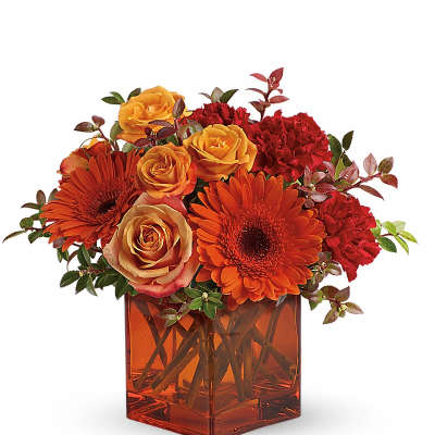 Compact orange and red bouquet of roses, gerbera daisies, and carnations in an orange glass cube vase