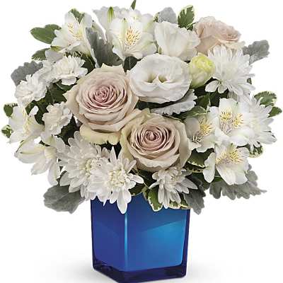 Compact arrangement of blush roses and white flowers in a blue glass cube vase