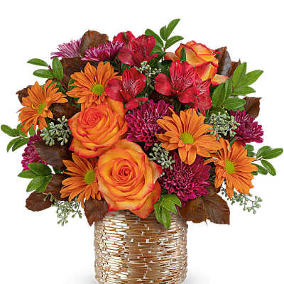 Short arrangement of orange roses, daisies, red alstroemeria and magenta mums in a gold woven vase